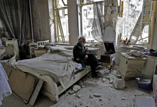 صورة السوري أبو عمر أثناء سماعه لموسيقاه المفضلة و هو جالسا داخل حجرته المدمرة من إندلاع الحرب السورية